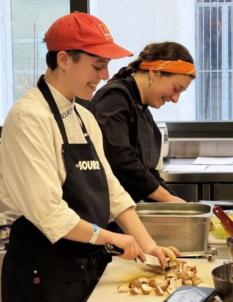 Une pâtissière en tablier blanc prépare des ingrédients dans un plan de travail en cuisine.