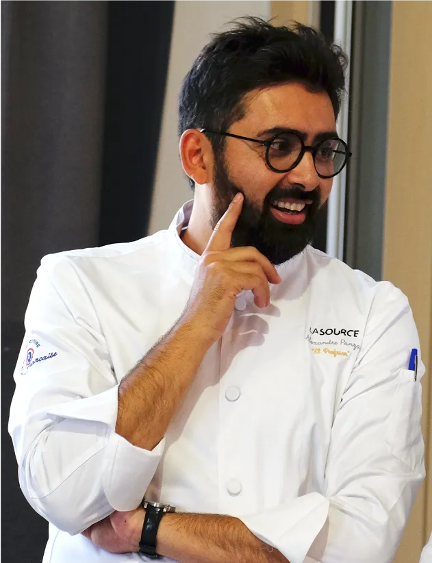 Jeune chef pâtissier en blouse blanche travaillant avec deux saladiers en acier inoxydable.