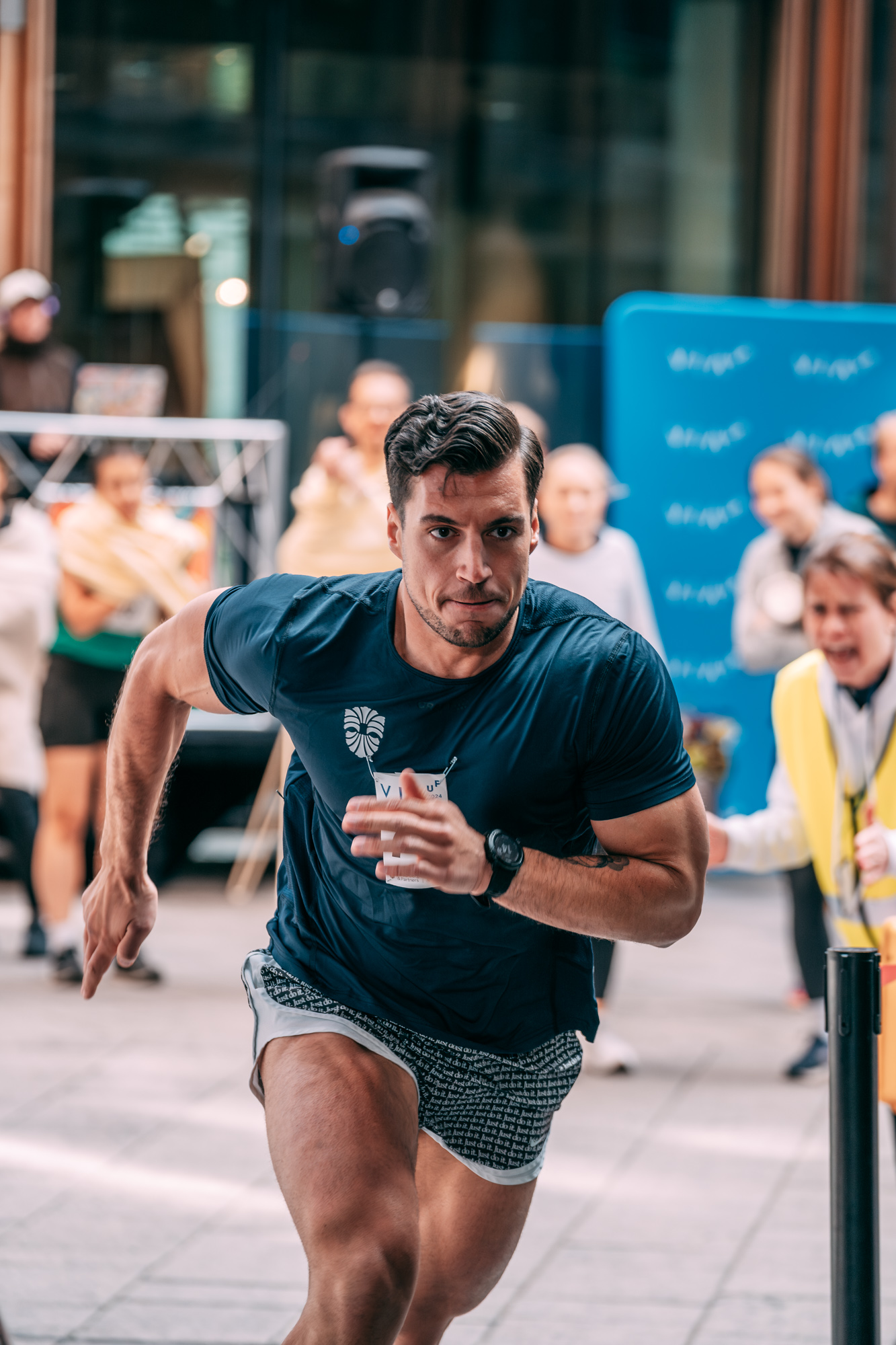 Focused male athlete sprinting indoors with a crowd watching and cheering behind him.