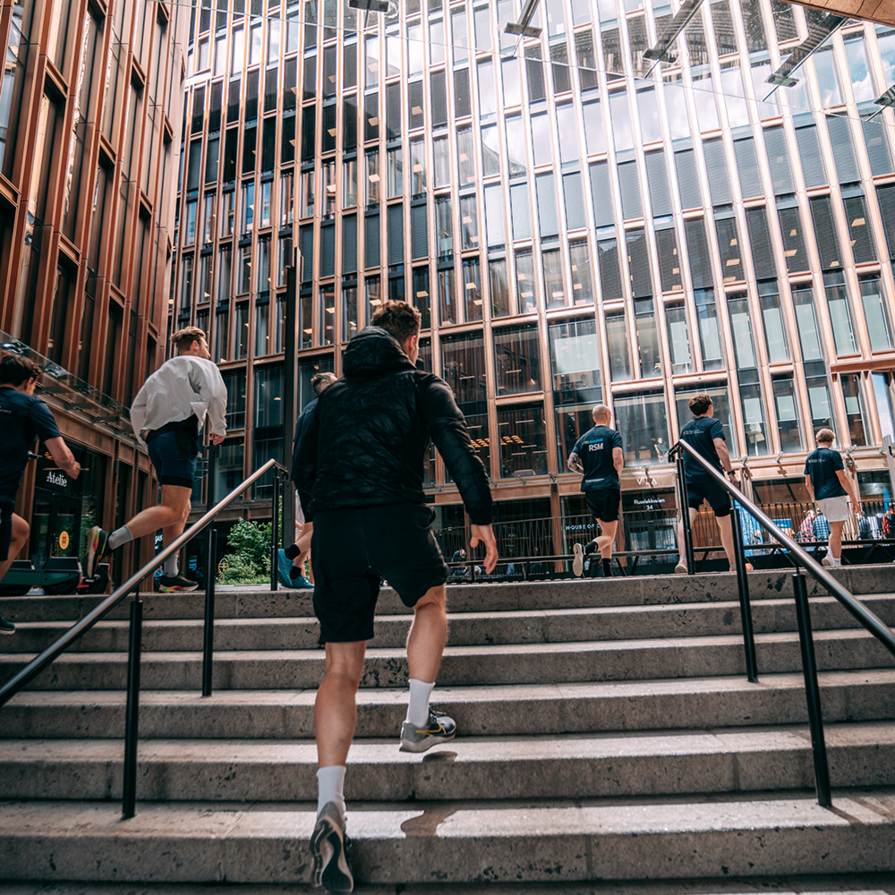 Group of people running up steps in an urban area surrounded by tall glass and metal buildings.