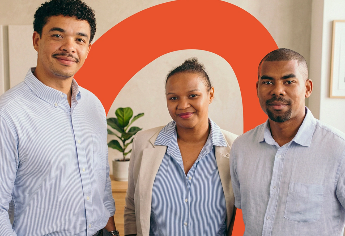 Trois personnes souriantes debout, deux hommes et une femme, avec plante et forme orange en arrière-plan.