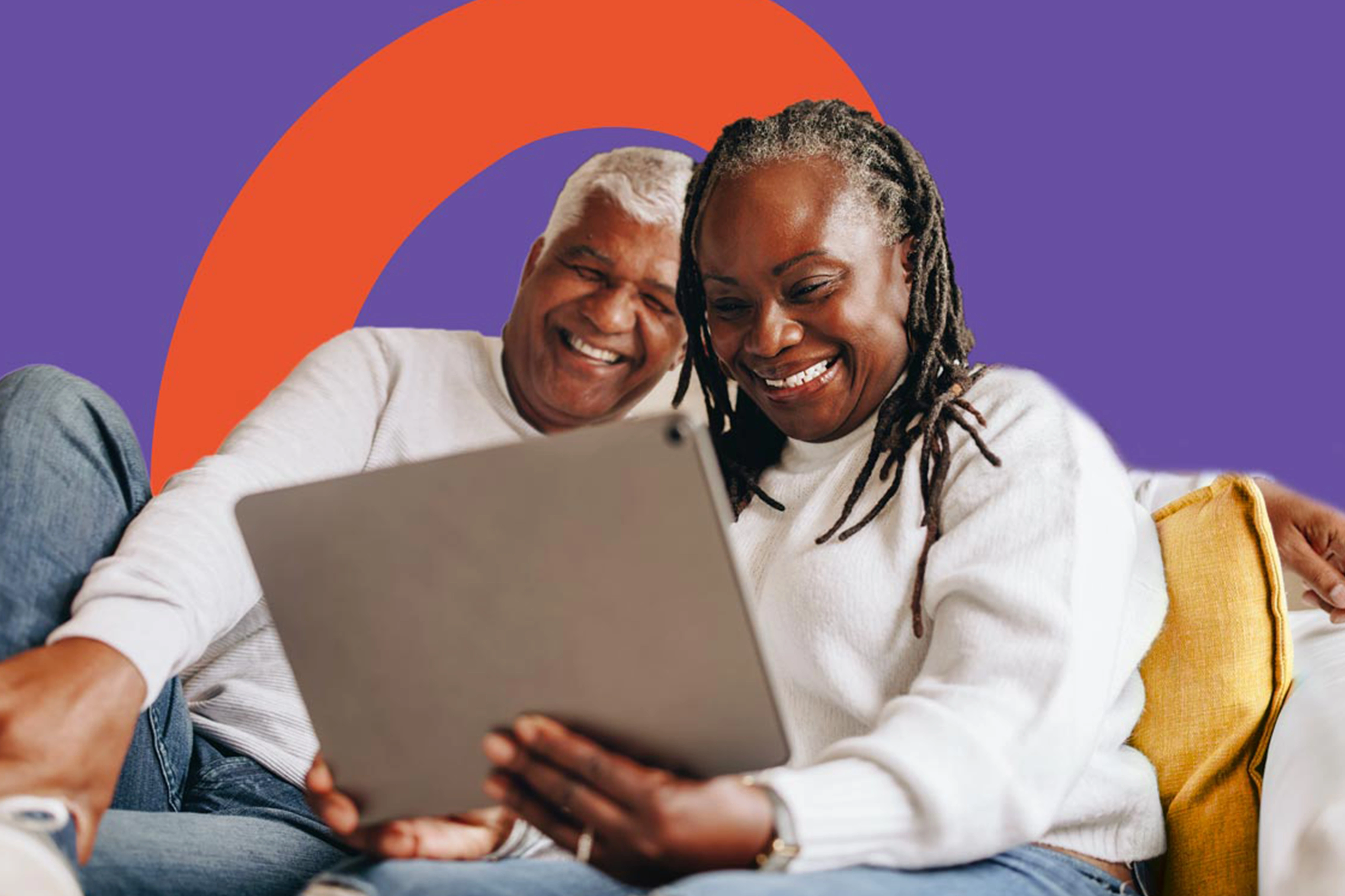 Couple souriant utilisant une tablette sur un canapé avec un coussin jaune, fond violet et orange.