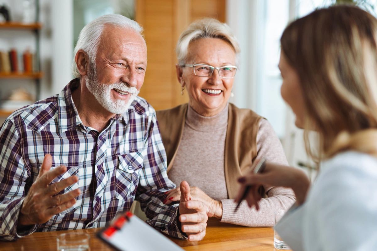 Couple de personnes âgées souriant en conversation avec une femme lors d'une consultation.