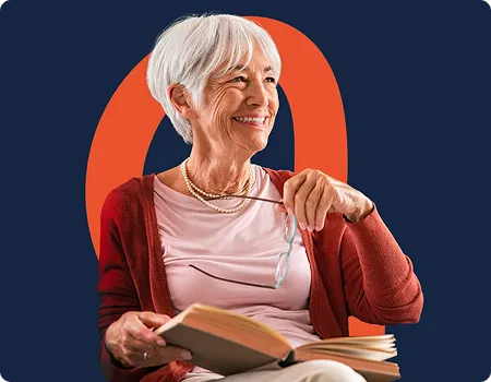 Femme âgée souriante tenant un livre ouvert et des lunettes dans un pull rouge.