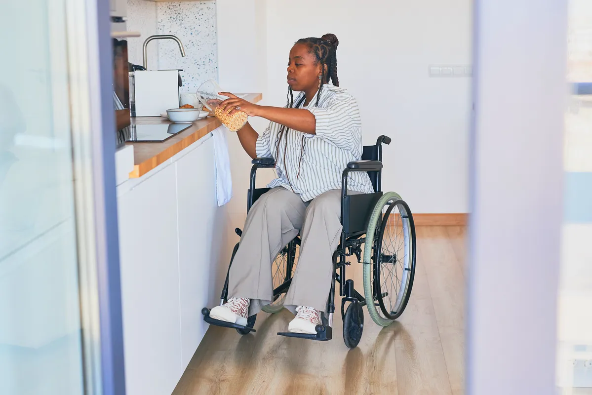Une femme en fauteuil roulant prenant un récipient de céréales dans une cuisine moderne.