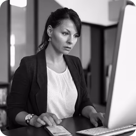 Person wearing a sweater typing on a laptop at a wooden table.