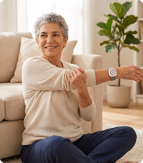 Femme souriante assise par terre, étirant son bras devant un canapé avec une smartwatch.