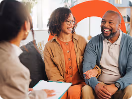 Un couple souriant assis avec un conseiller lors d'une réunion informelle au bureau.