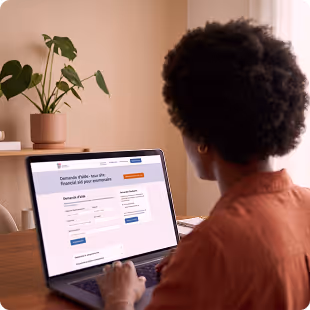 Person using laptop at desk with potted plant nearby, working on a form or application webpage.