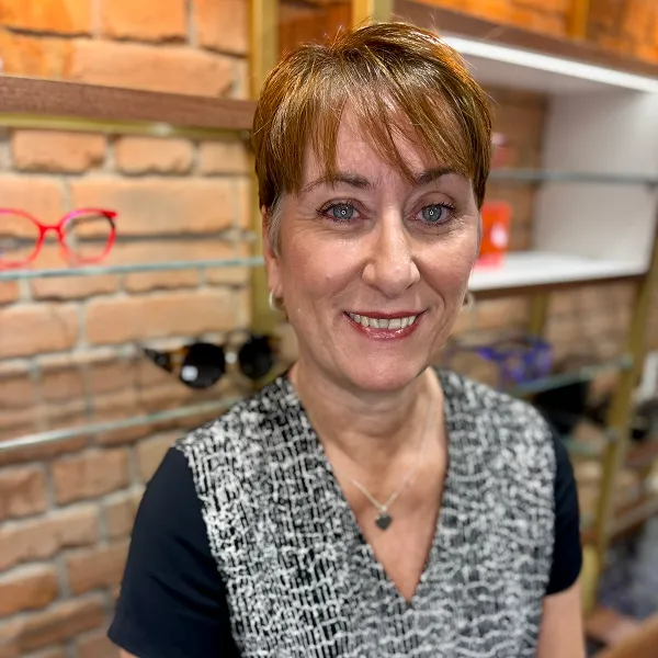 Smiling woman with short hair wearing a patterned top in a store with a brick wall background.