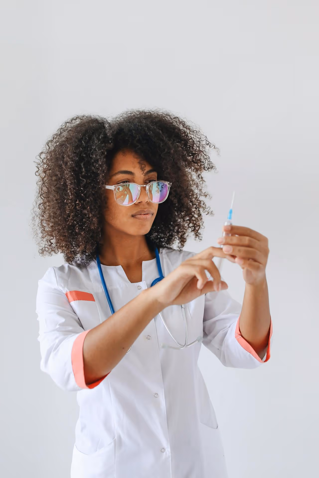 Female healthcare professional with curly hair and reflective glasses preparing a syringe.