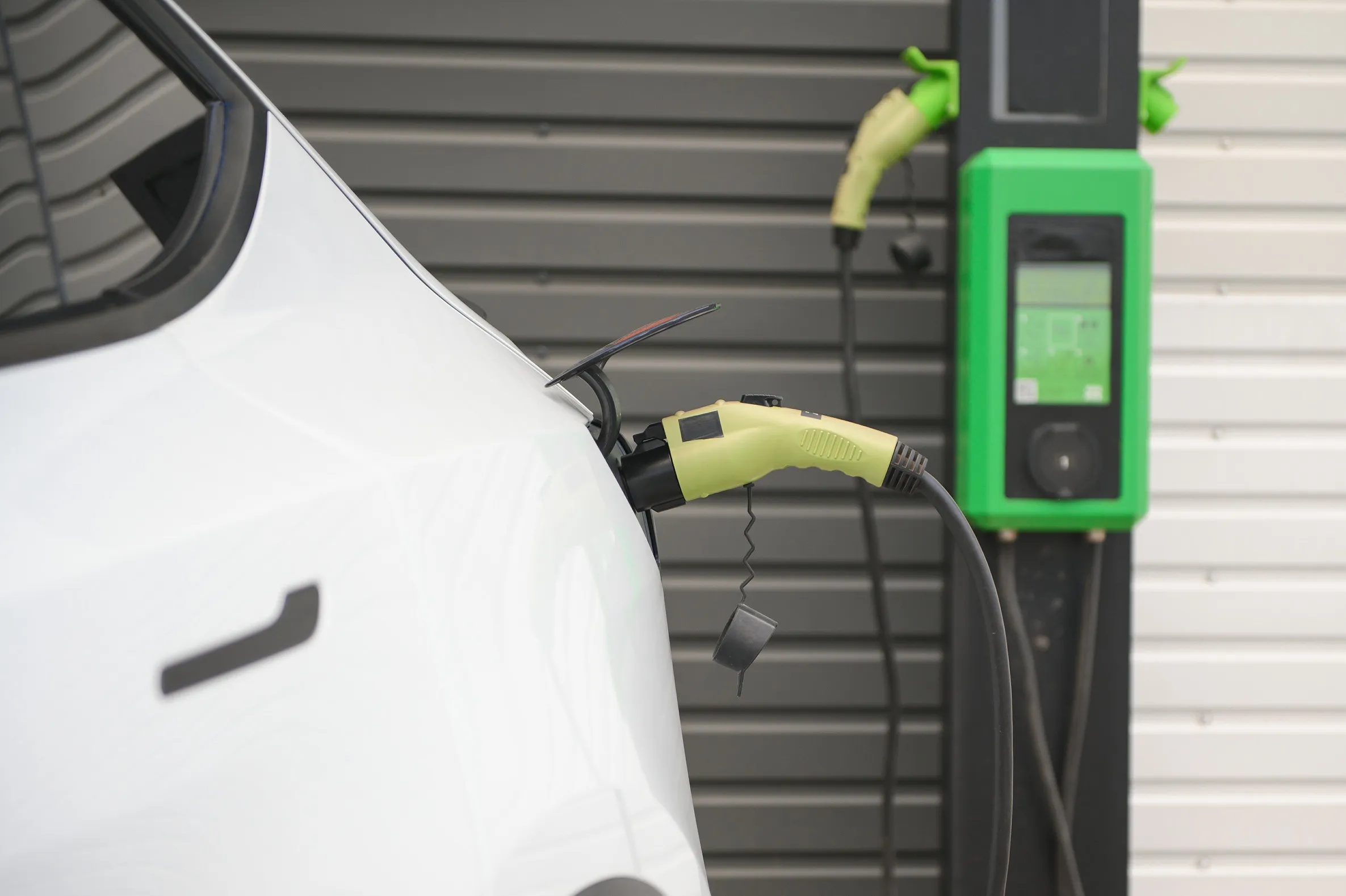 A parked electric car charging from a wall-mounted home charging unit