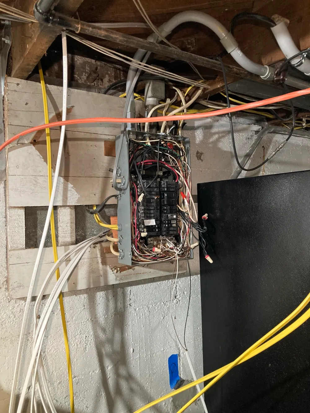 An unfinished electrical panel mounted on a basement wall in Arlington