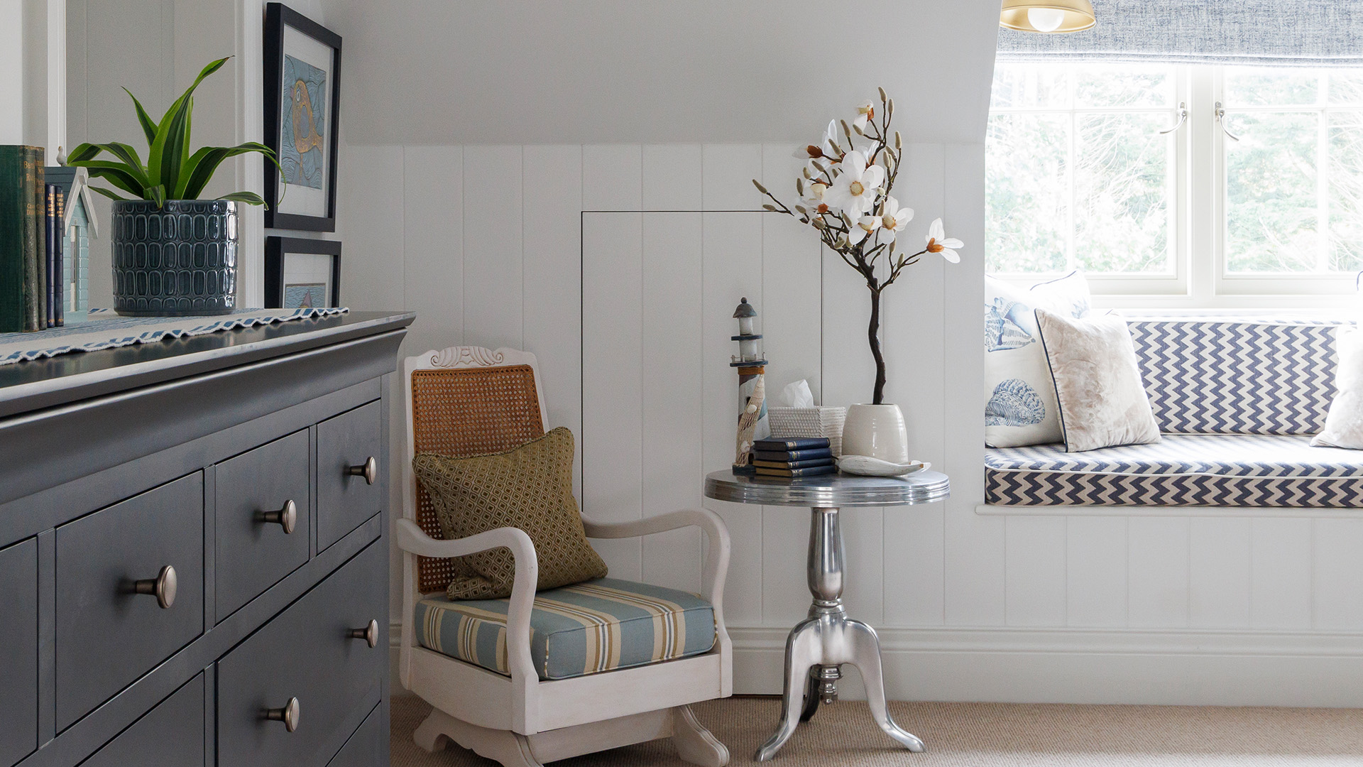 Panelled window seat with patterned cushions beside a grey painted chest of drawers