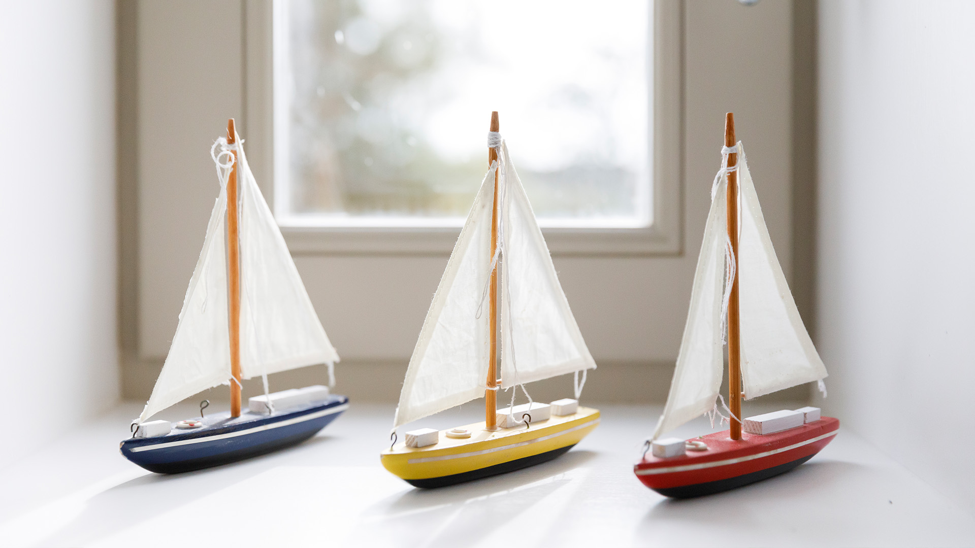 Trio of model sailing boats on a bright windowsill