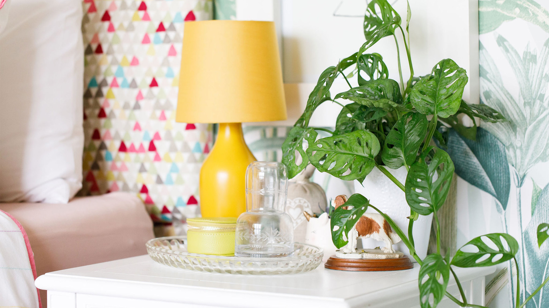 Yellow bedside lamp and houseplant against colourful geometric wallpaper