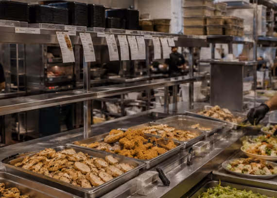 Buffet line with trays of cooked chicken and fried food in a commercial kitchen setting.