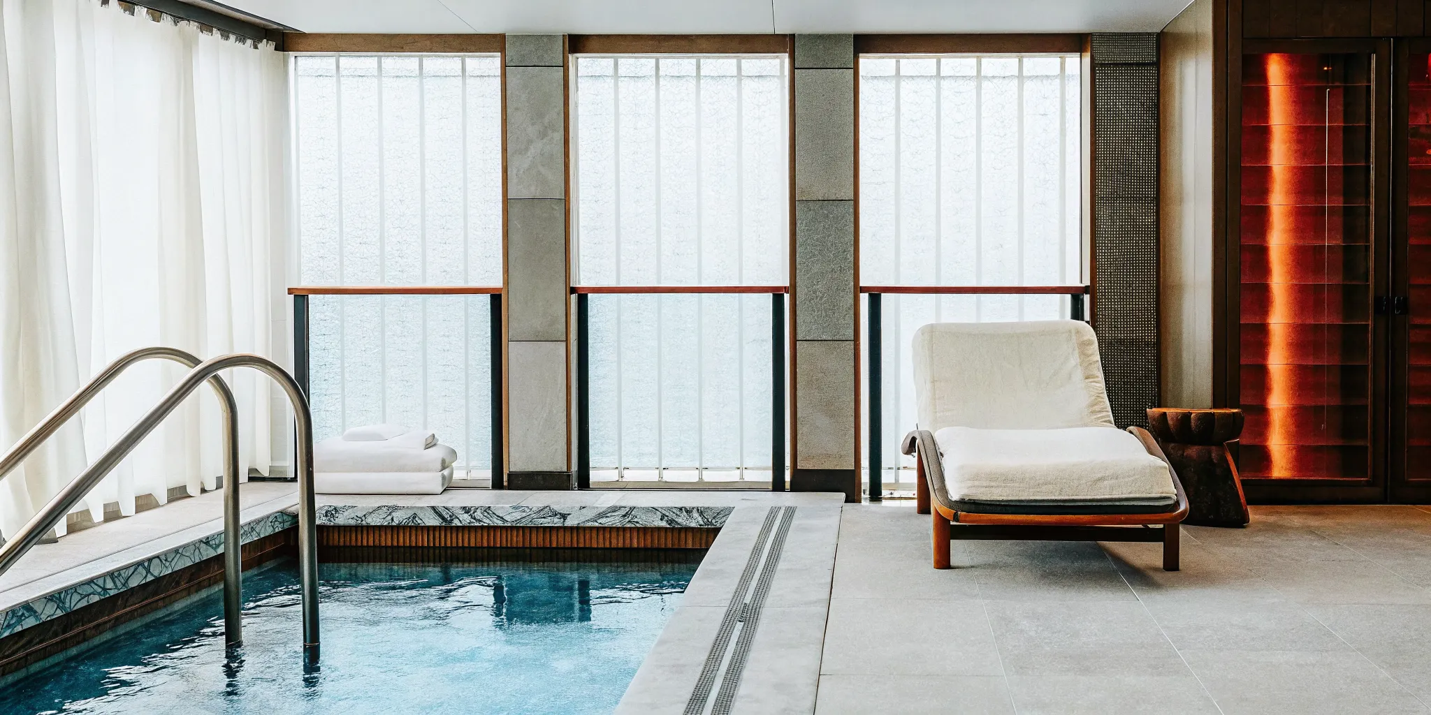 Modern Altea recovery lounge featuring a cold plunge pool with soft blue lighting, red light therapy panels, and compression boot recliners