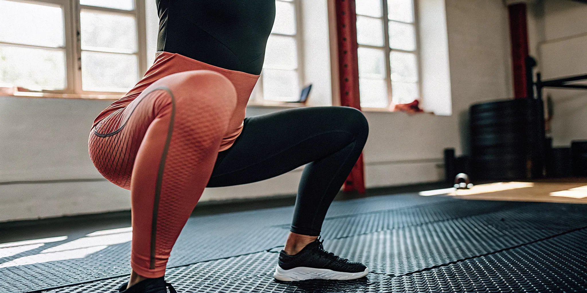 An athlete demonstrating mobility training benefits with a deep, controlled squat in a brightly lit premium club.