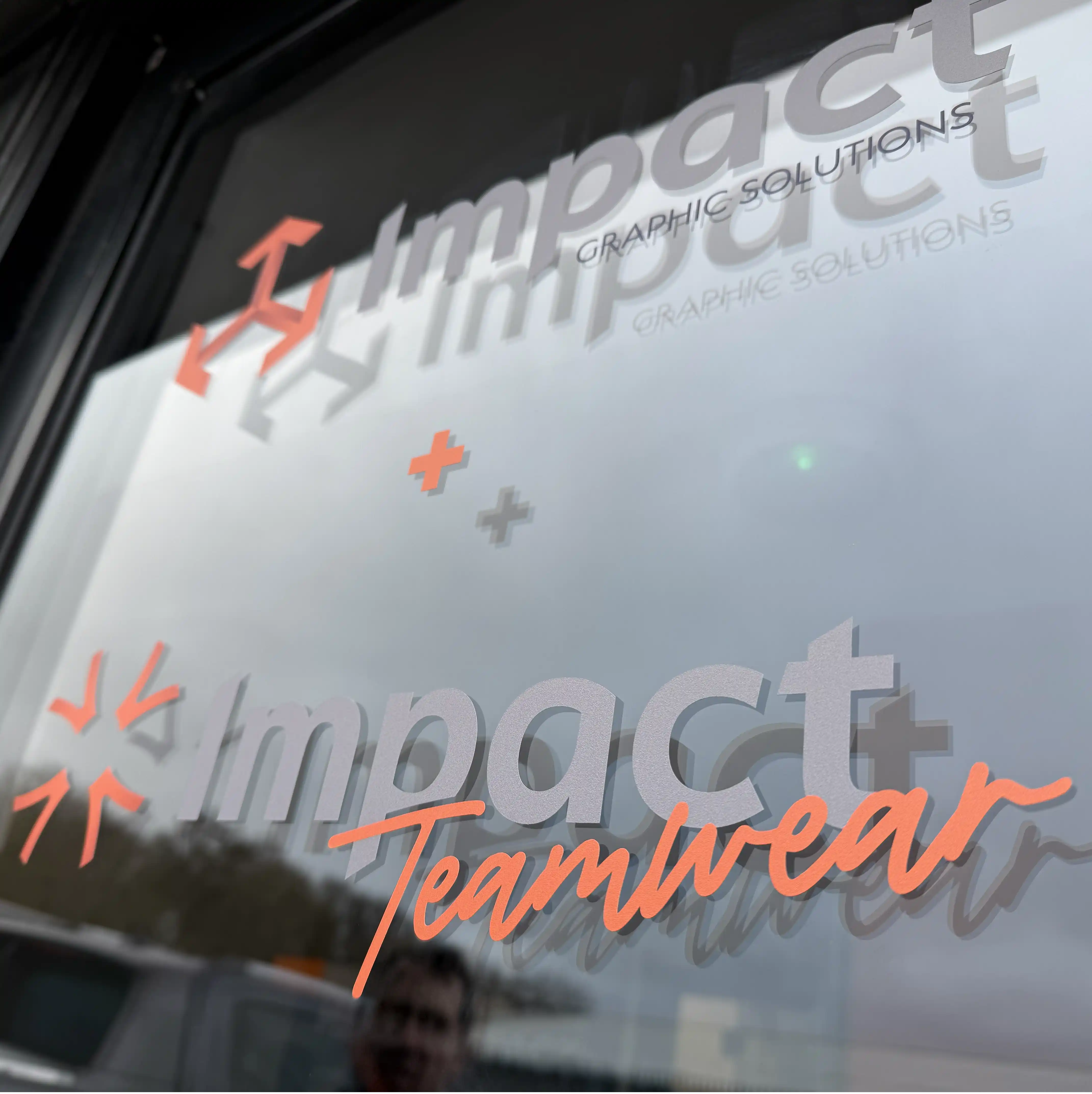 Photo of a window graphic showing both the Impact Design & Print and Impact Teamwear logos at their production unit in Basingstoke UK