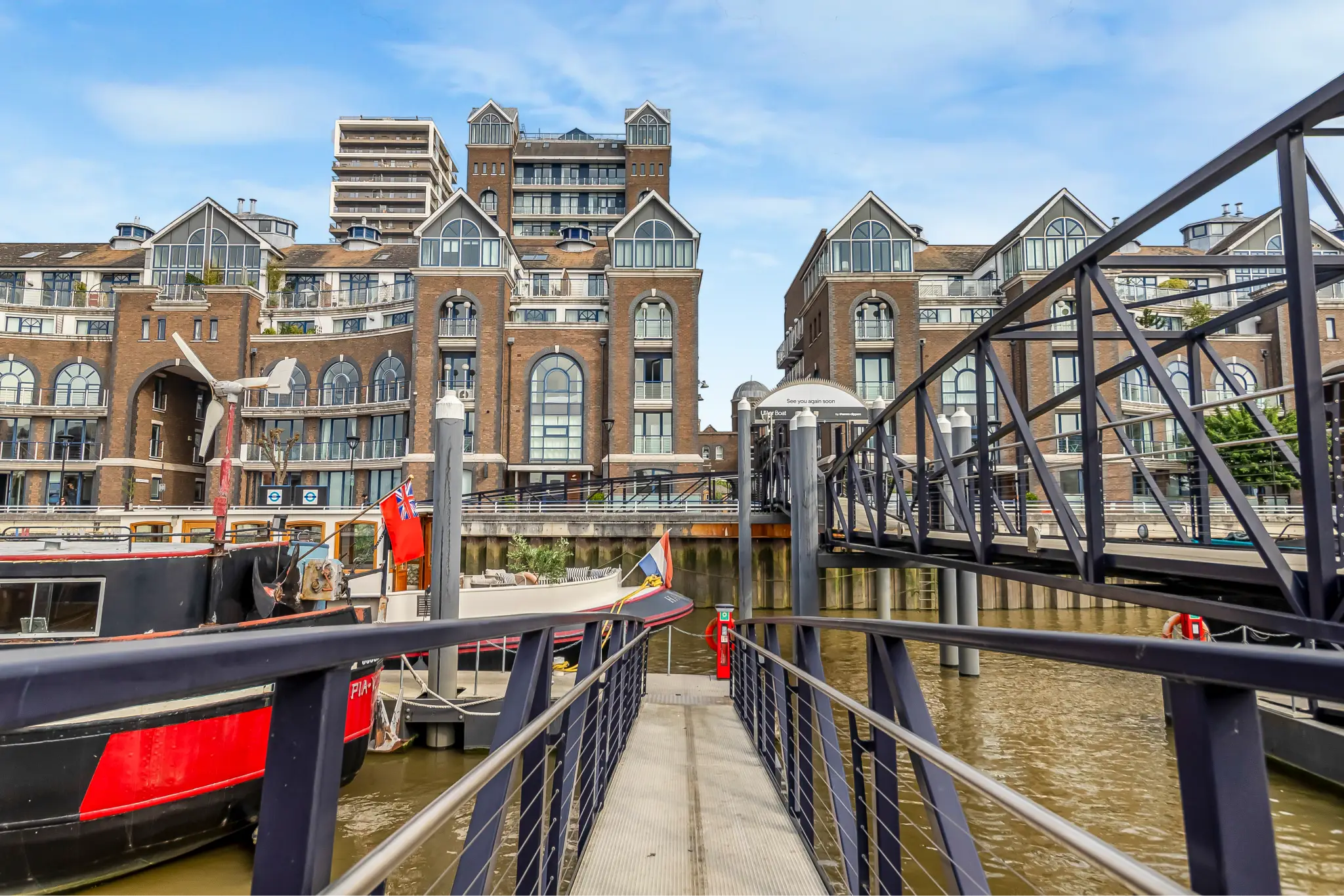Dock walkway leading to moored boats with brown brick apartment buildings in the background.