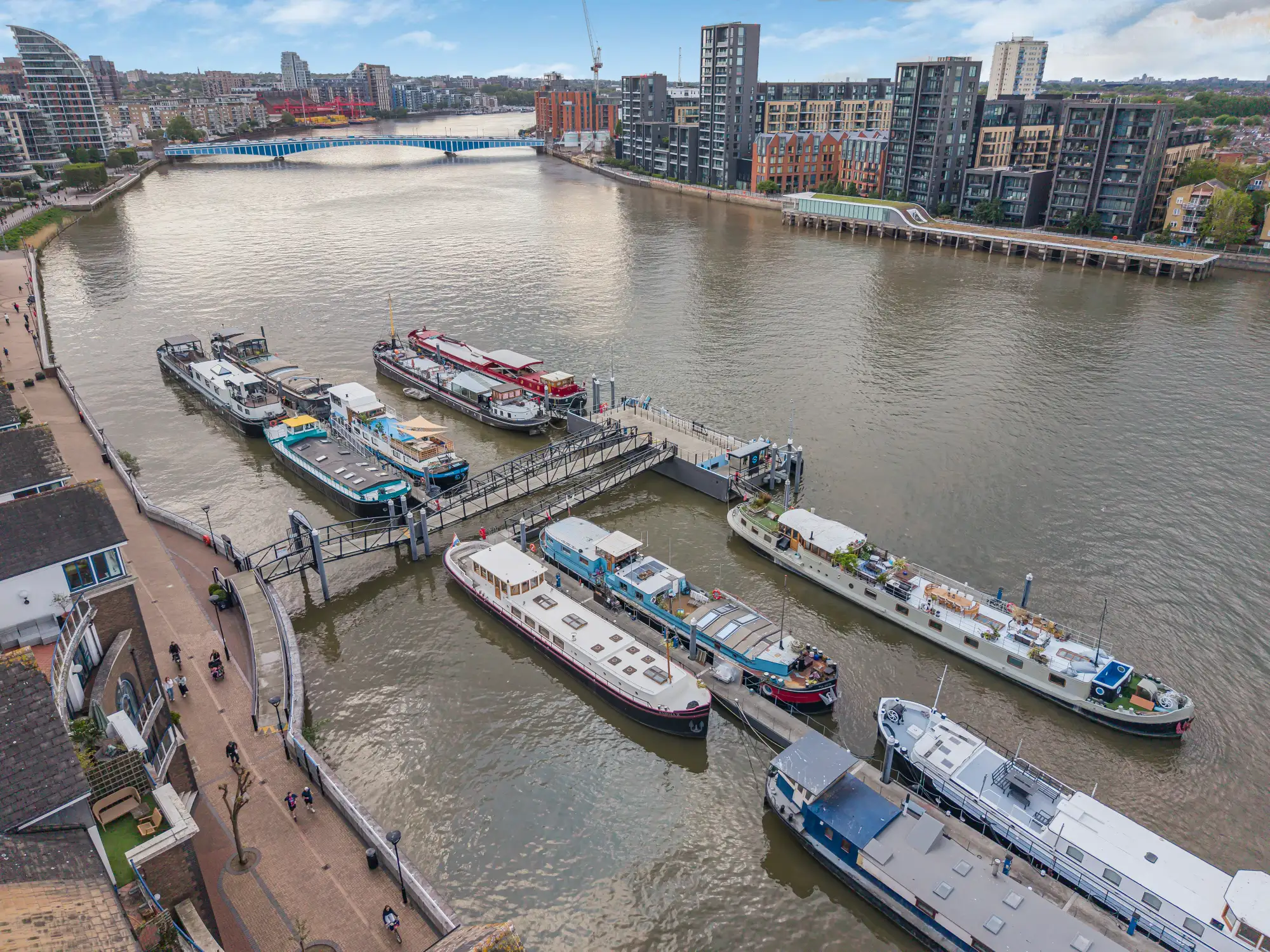 A river marina with multiple docked boats and modern residential buildings along the water.