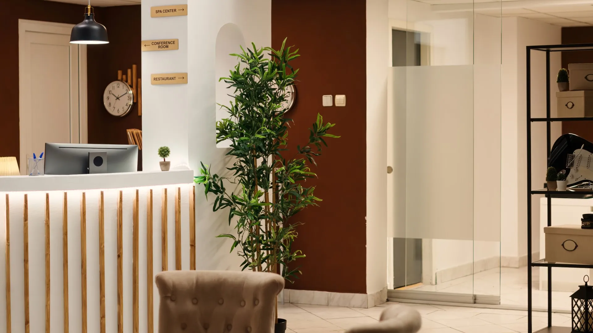 Reception desk with computer, indoor plant, clock, and signs for spa, conference room, and restaurant.