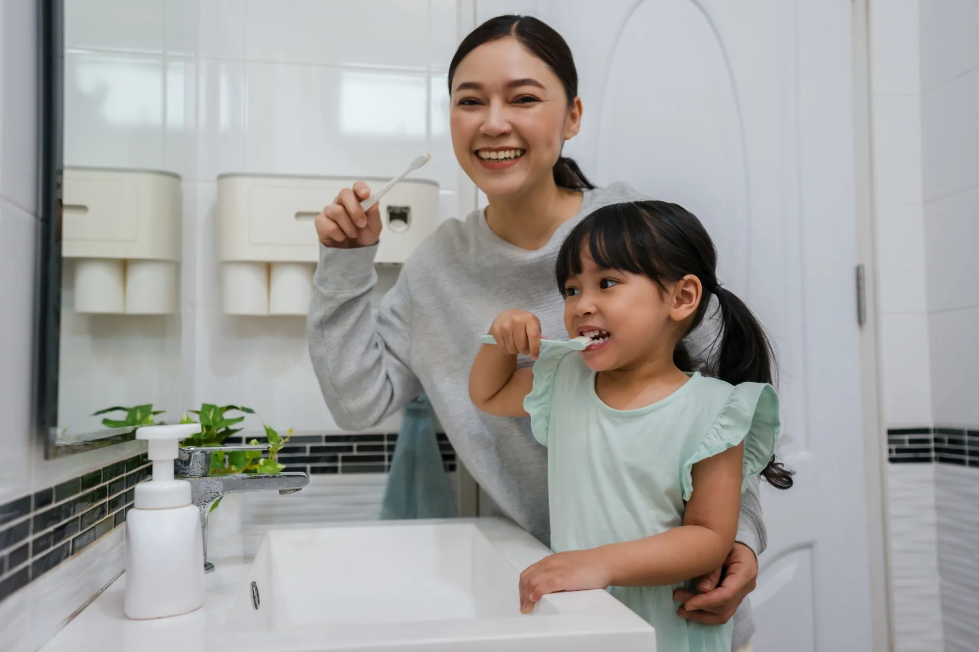 Mother and daughter smiling while brushing their teeth together in a bathroom.