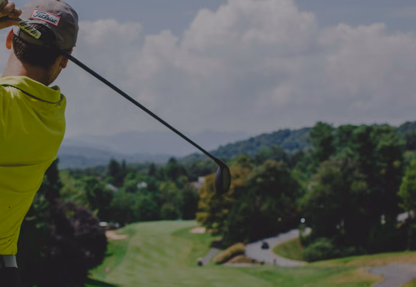 Man in green shirt swinging a golf club at a driving range.