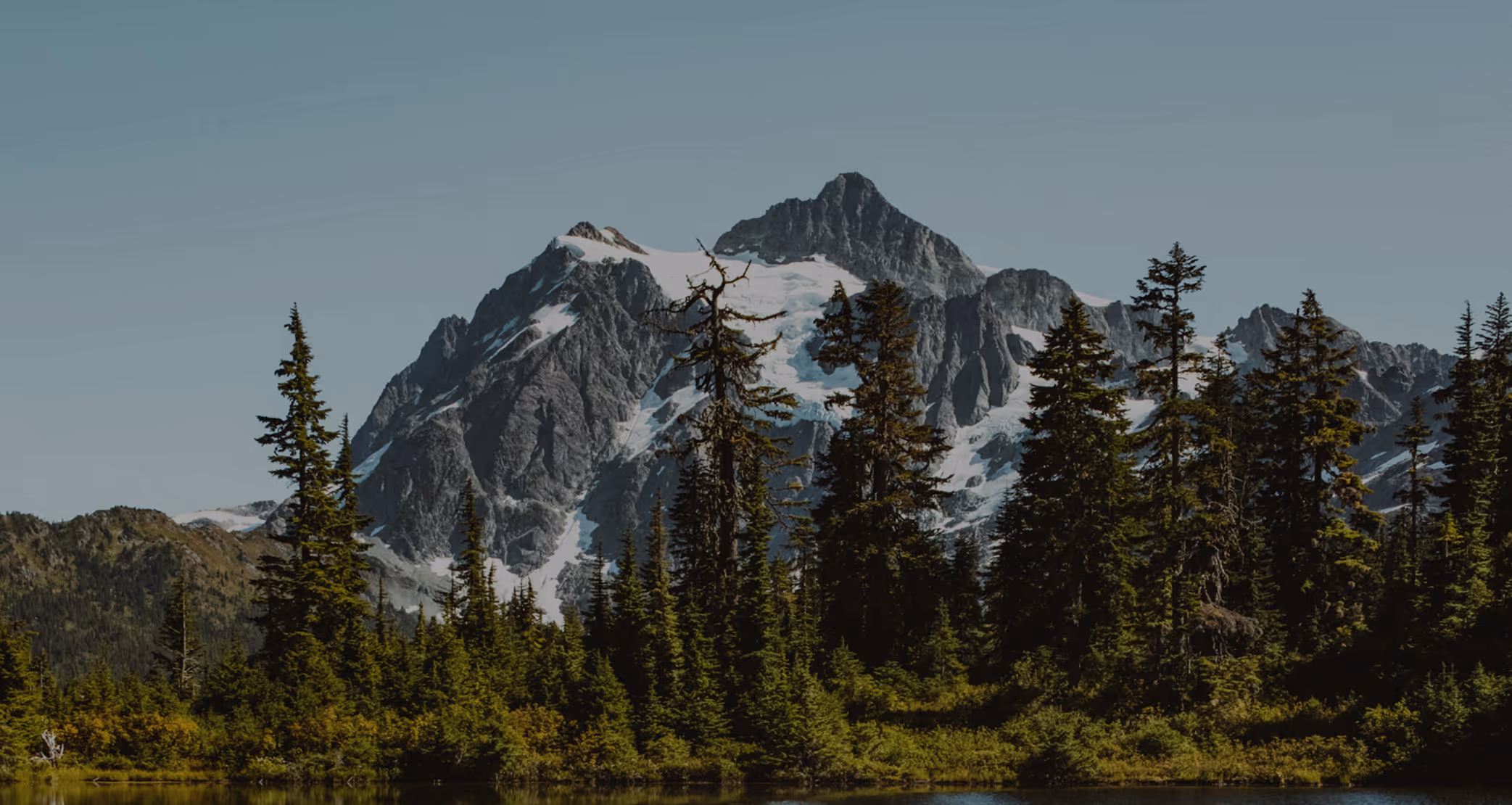 White capped mountains surrounded by pine trees.