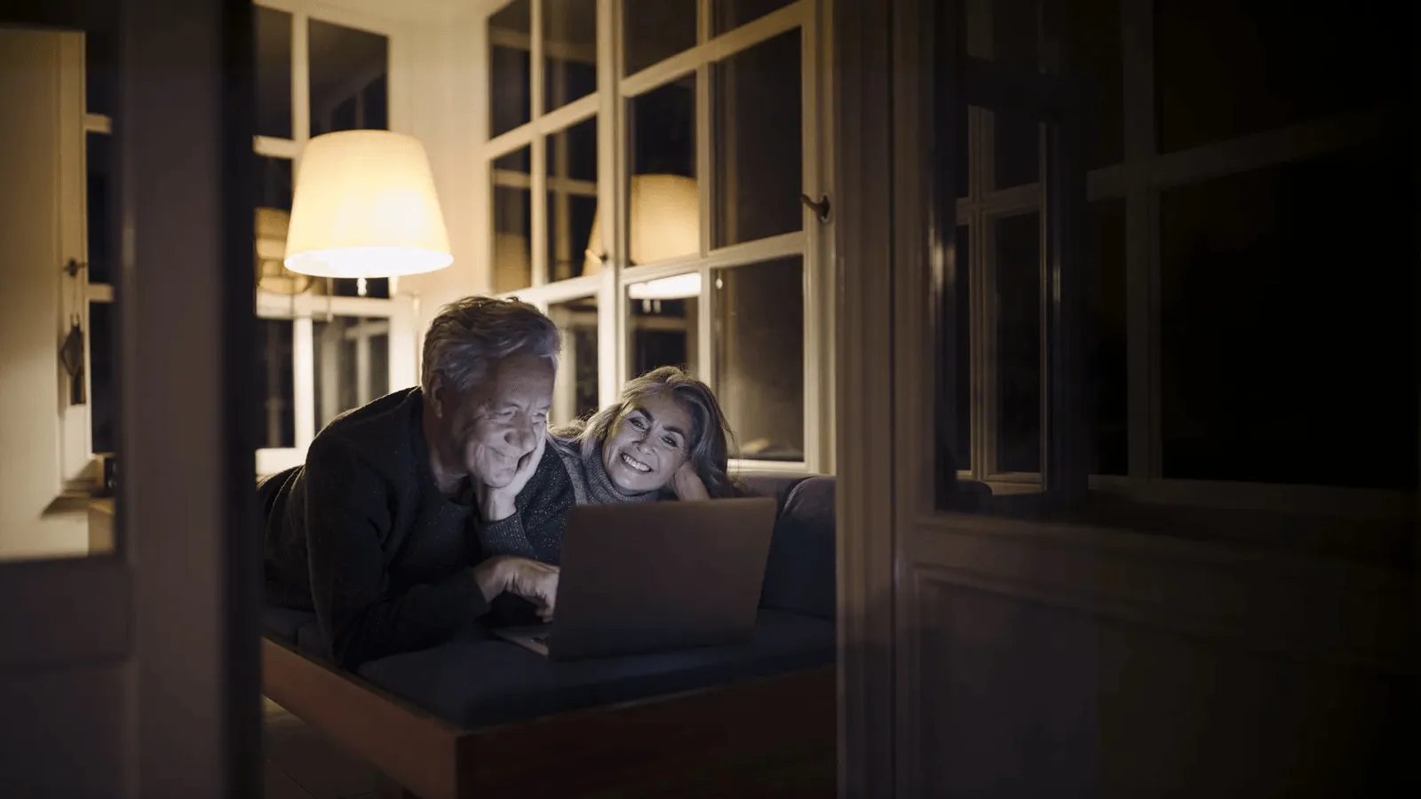 Ein älteres Paar sitzt auf einem Sofa und schaut auf ein Laptop.