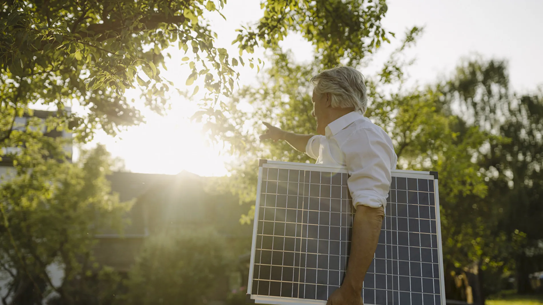 Mann trägt Solarpanel unter dem Arm und zeigt auf ein Haus.