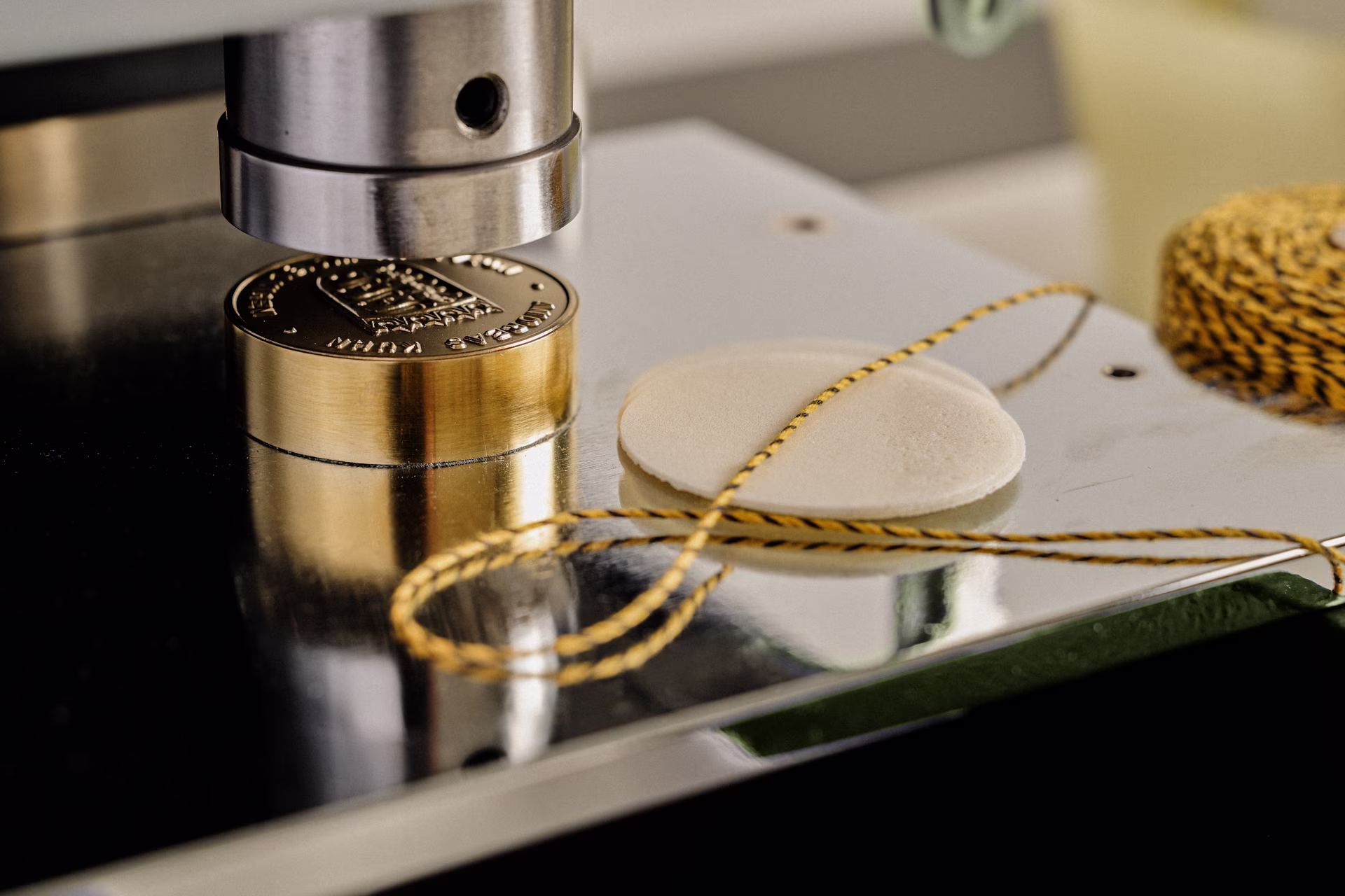 Prägemaschine prägt ein rundes goldenes Medaillon auf einer glänzenden Metallfläche.
