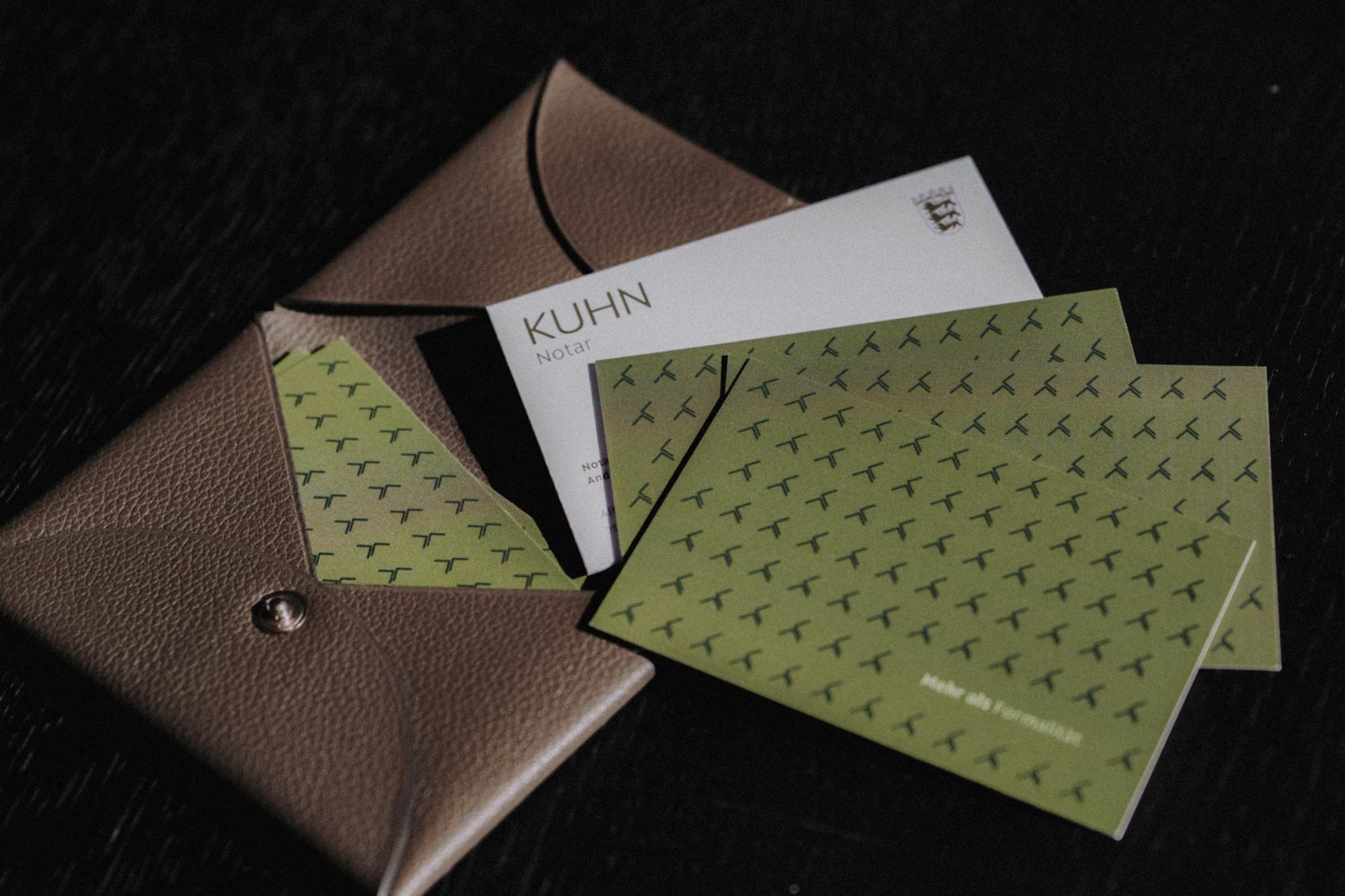 Braune Ledertasche mit weißen und grünen Visitenkarten von Notar Kuhn darauf.