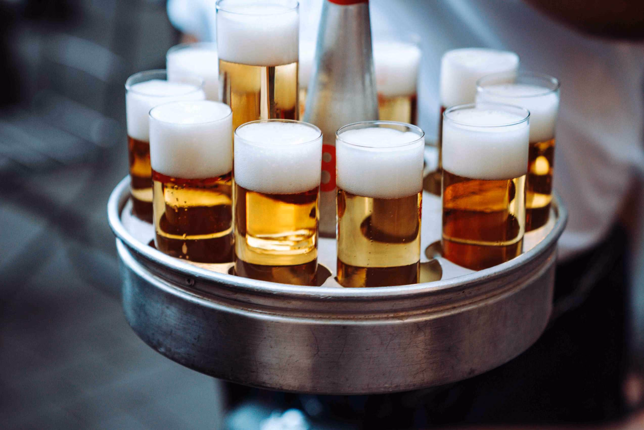 Köbes trägt rundes Tablett voll mit frisch gezapften Kölsch-Gläsern durchs Brauhaus