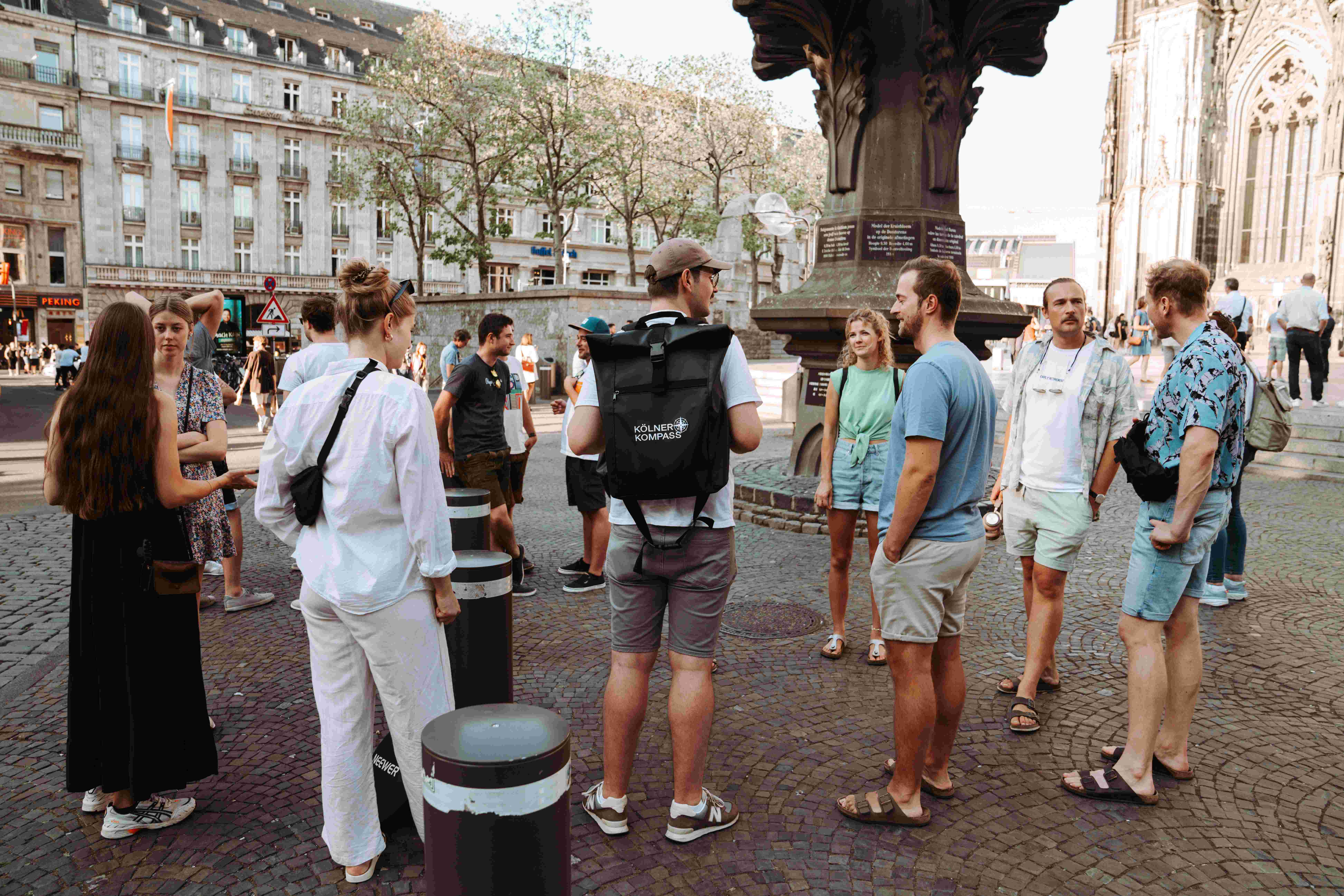 Mehrere Menschen stehen in einem Kreis auf einem gepflasterten Platz vor einem historischen Gebäude.