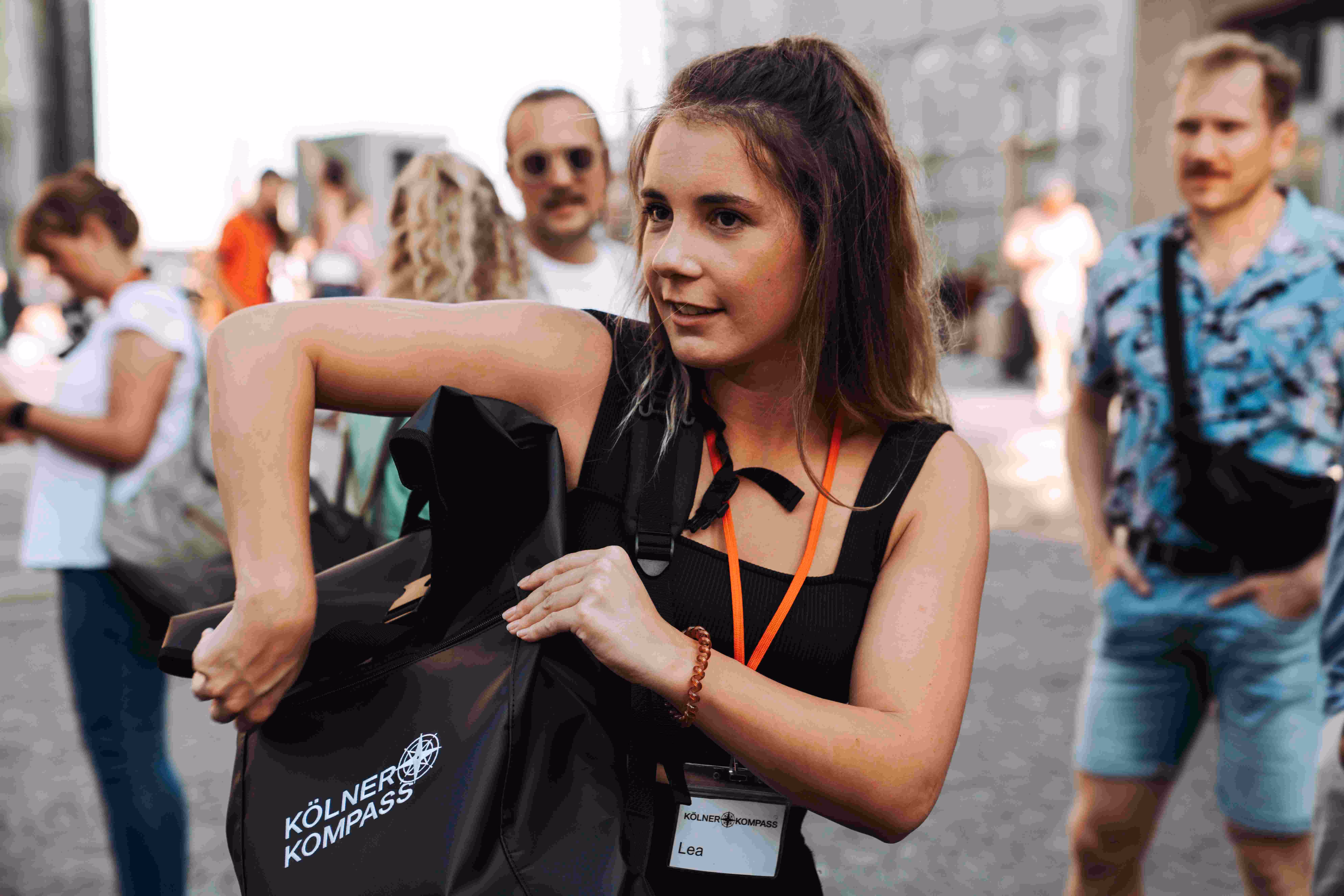 Kölner Kompass Tourguide holt etwas aus dem Rucksack mit Logo auf der Domplatte