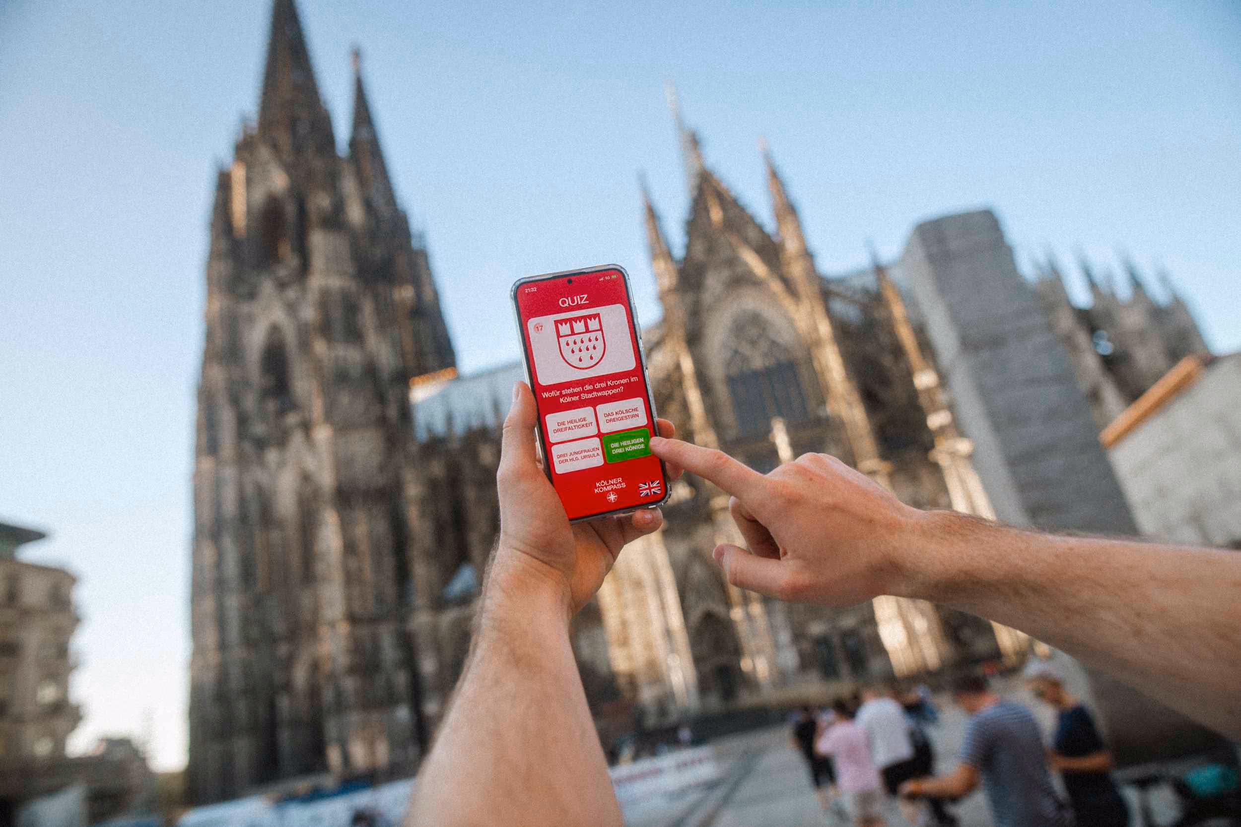 Handy mit Stadtrallye Köln App wird vor dem Kölner Dom gehalten