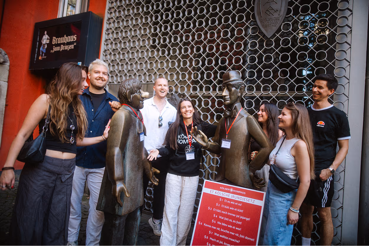 Kölner Kompass Tourguide steht mit Gästegruppe bei der Tünnes-und-Schäl-Statue in Köln