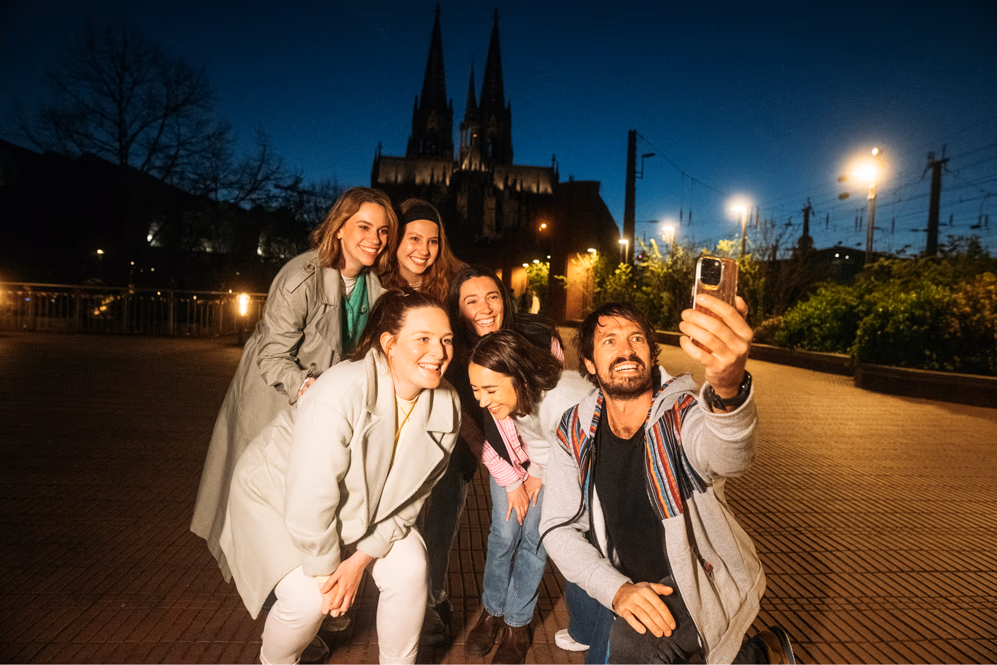 Gruppe macht ein Selfie vor dem beleuchteten Kölner Dom bei Nacht