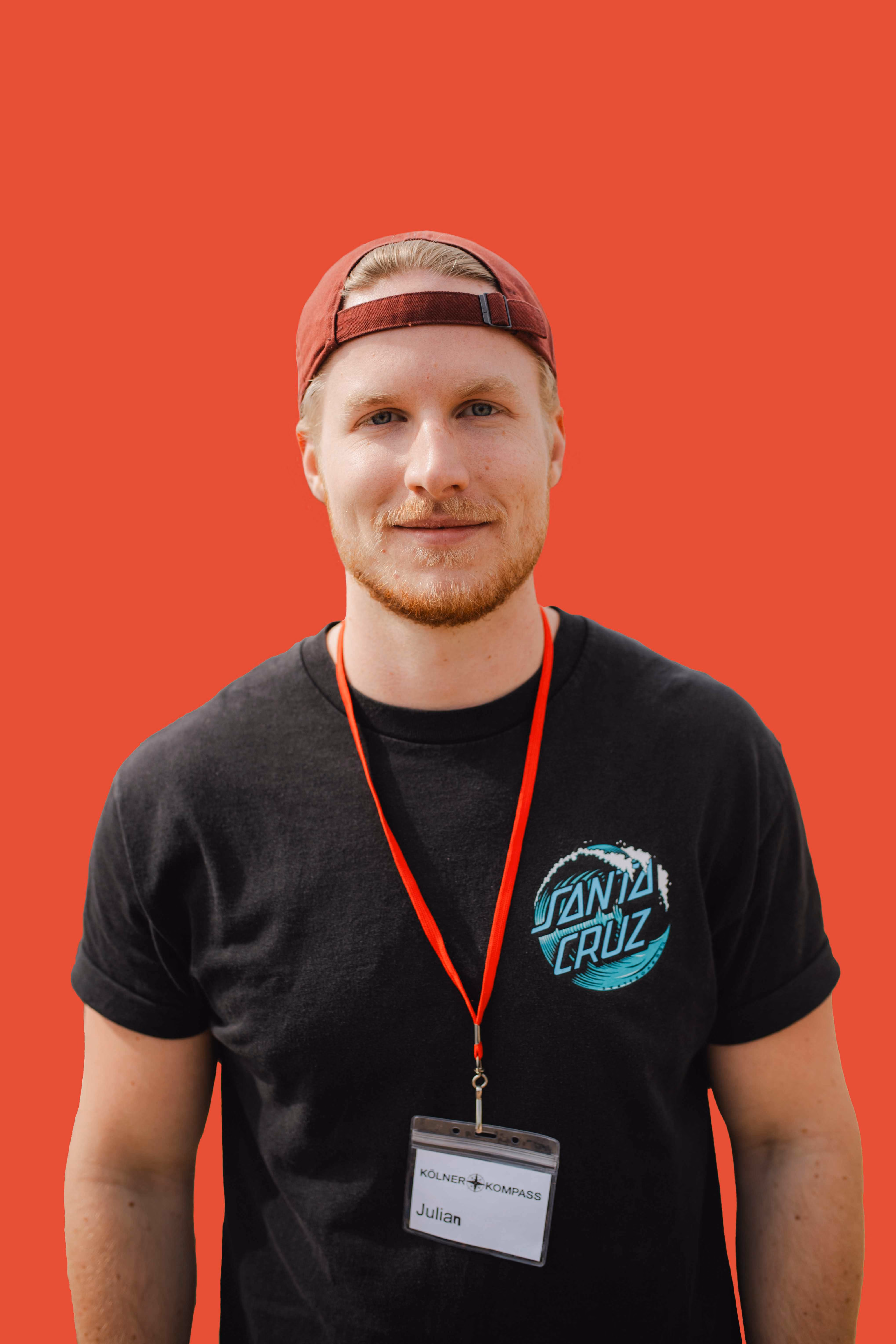 Kölner Kompass Tourguide mit Cap und Lanyard vor roter Wand