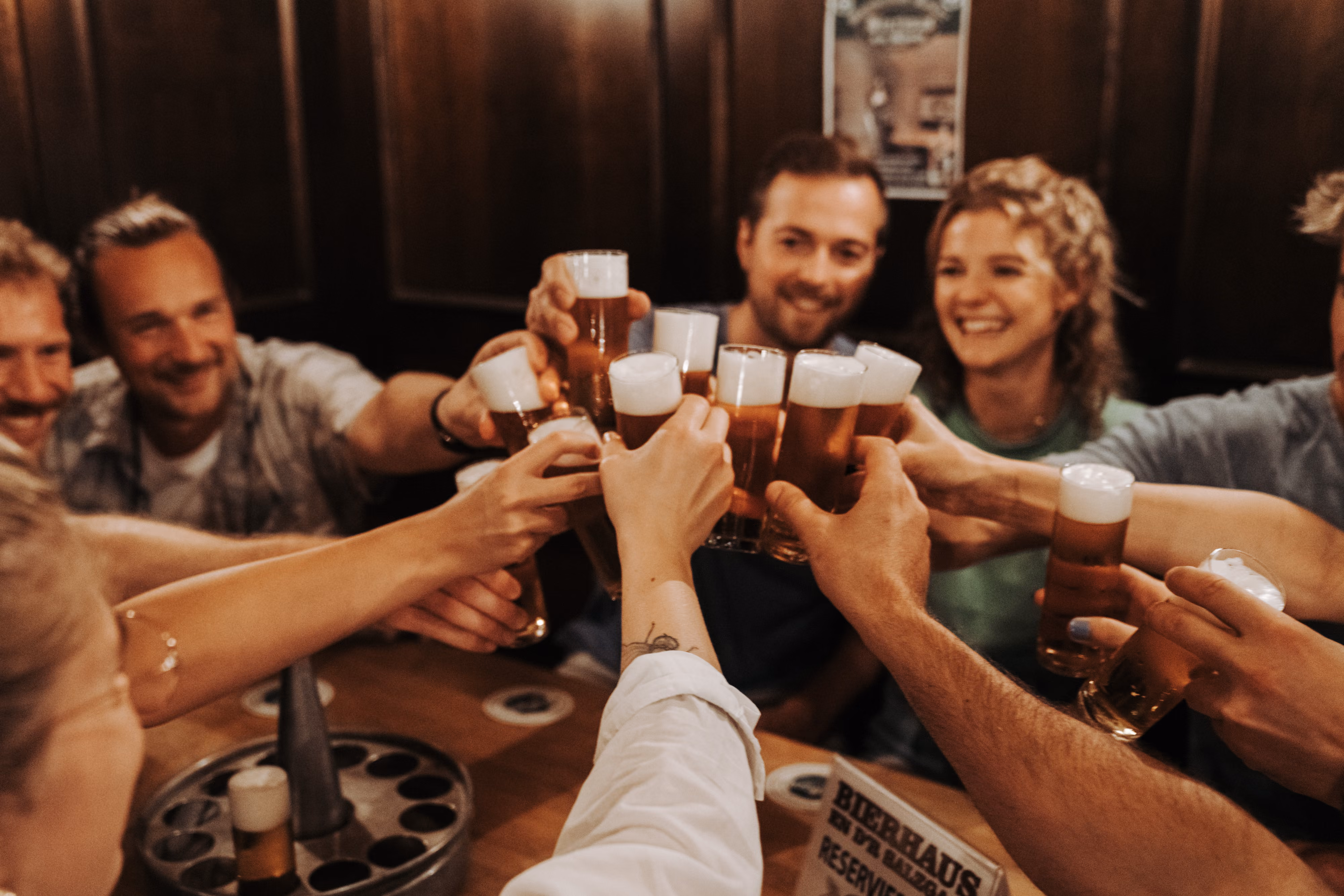 Größere Gruppe stößt gemeinsam mit Kölsch-Gläsern an einem Tisch im Brauhaus an