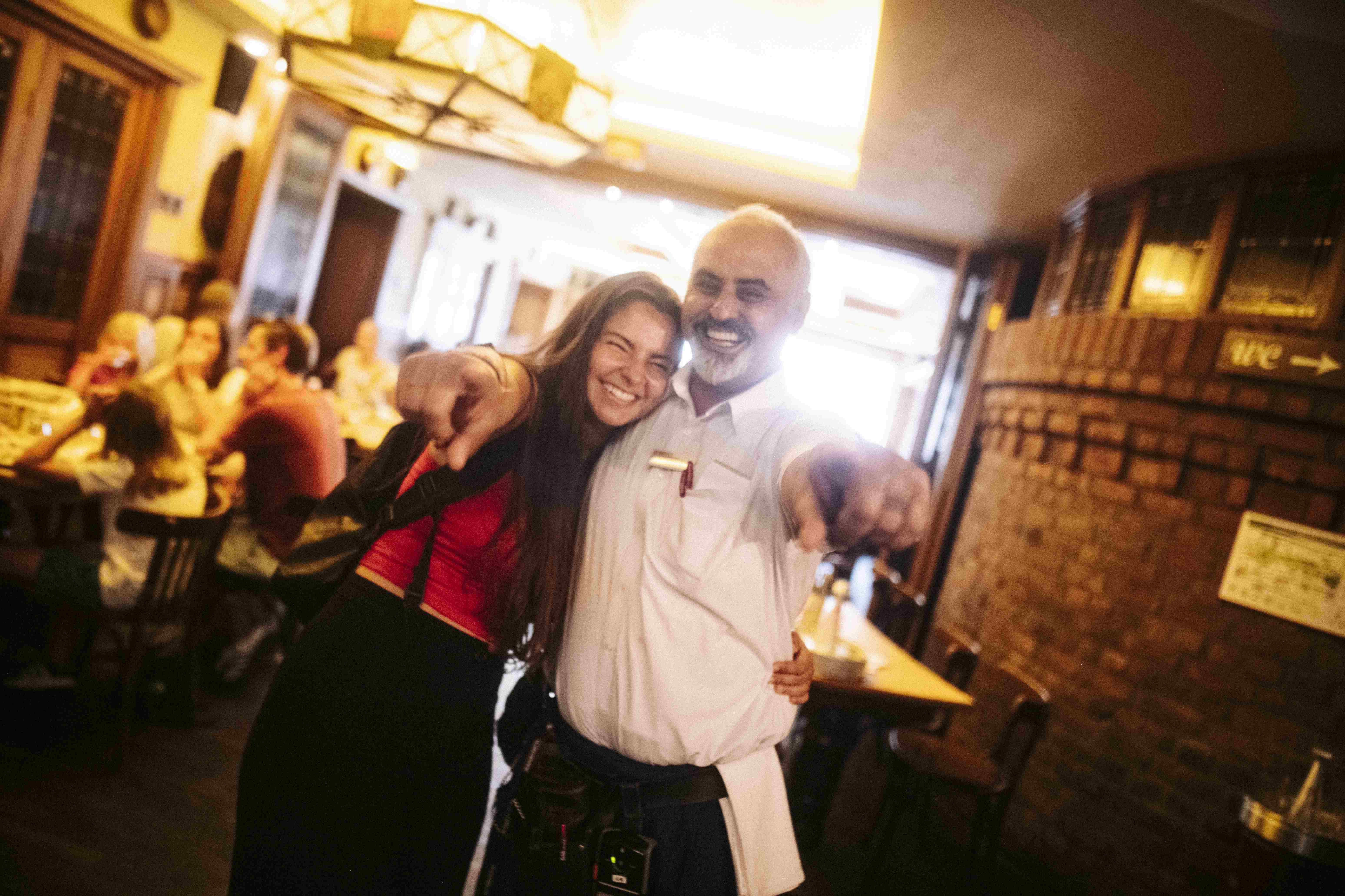 Lächelnde Frau und Mann umarmen sich und zeigen nach vorne in einem belebten Restaurant.