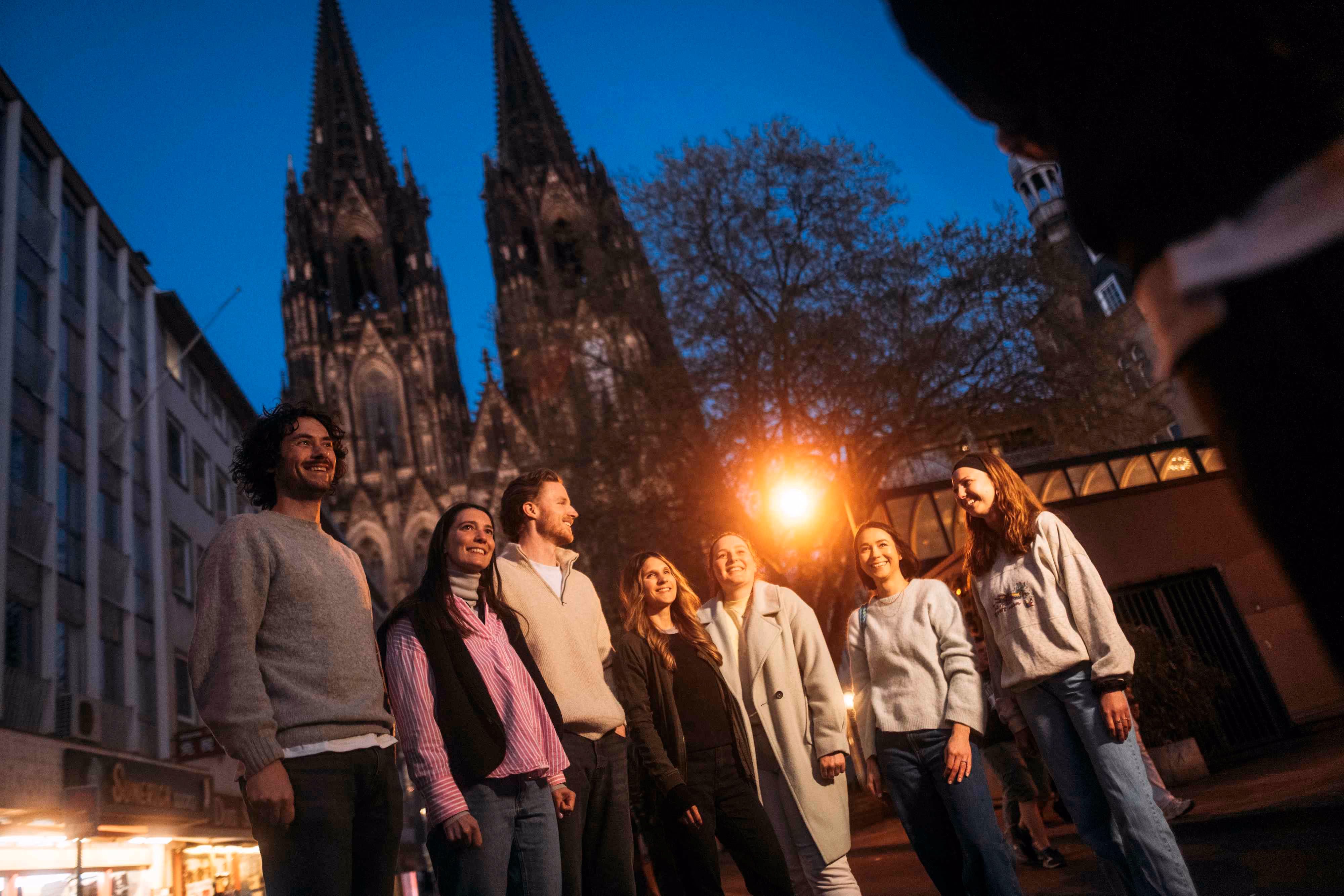 Gruppe steht abends vor dem beleuchteten Kölner Dom und blickt nach oben