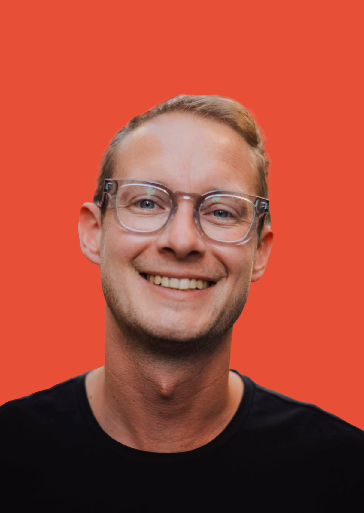 Ein lächelnder Mann mit klaren Brillengläsern vor rotem Hintergrund.