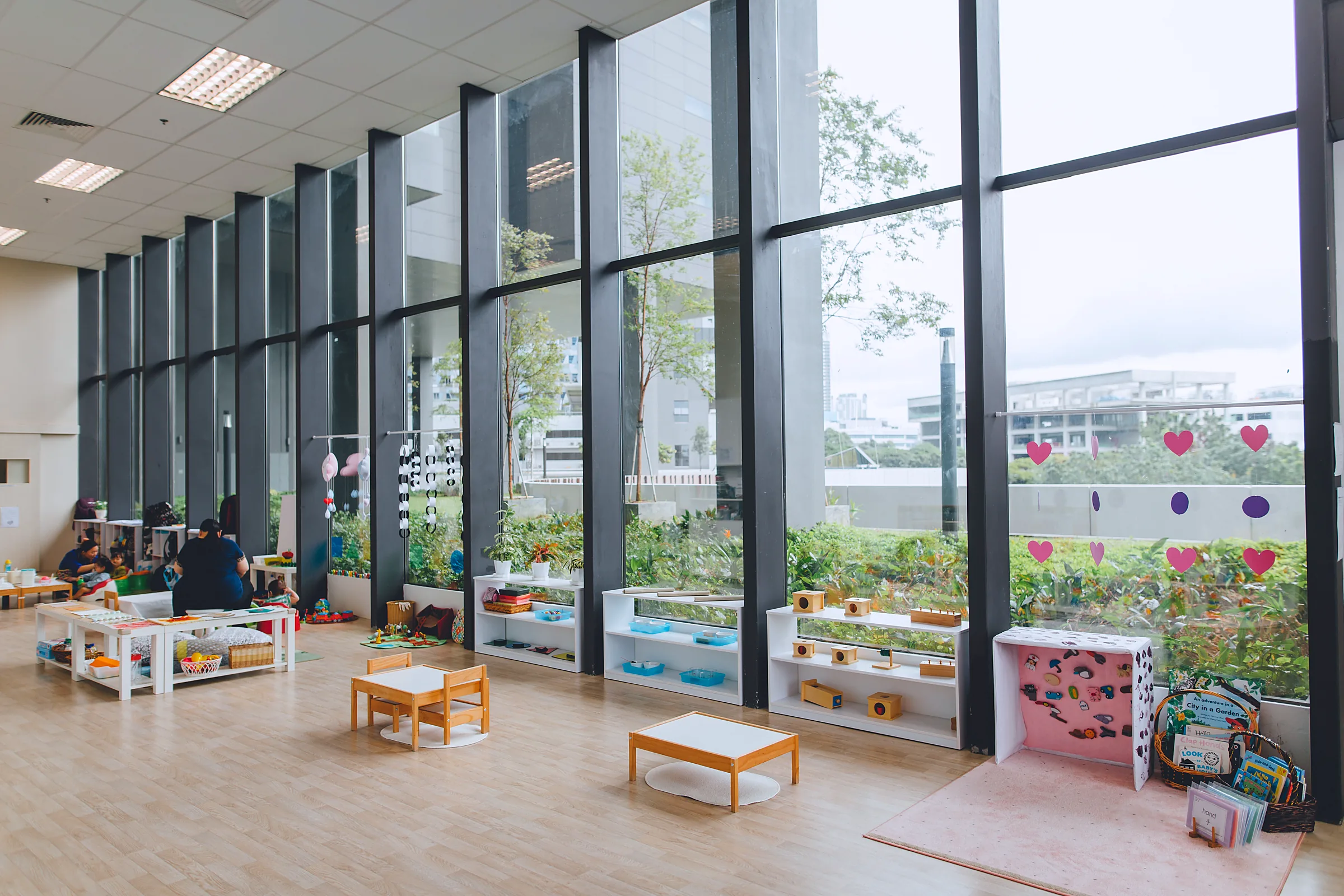 Calm, light-filled Montessori classroom with low shelves and floor-to-ceiling windows at Josiah
