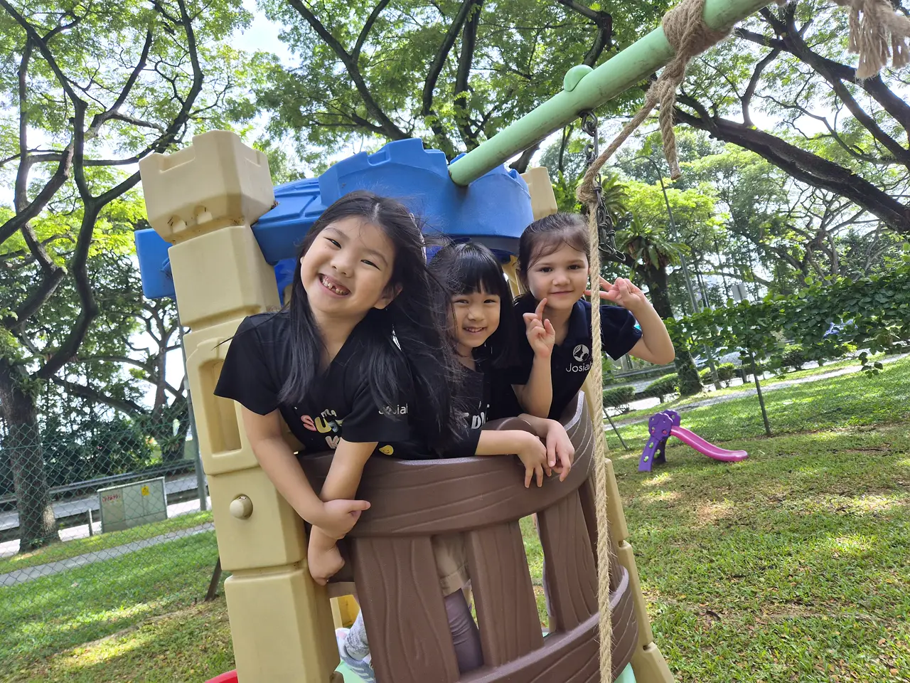 Three Josiah Montessori children playing together at an outdoor playground.