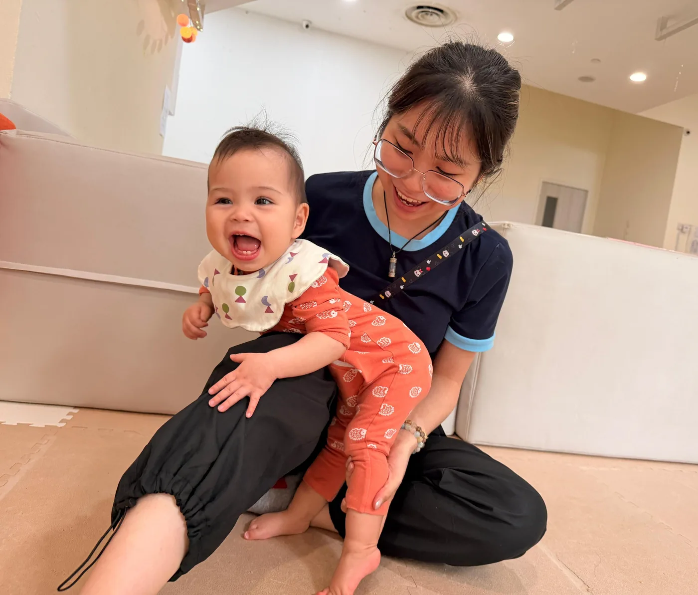 A Josiah educator supporting a laughing baby taking weight on both feet