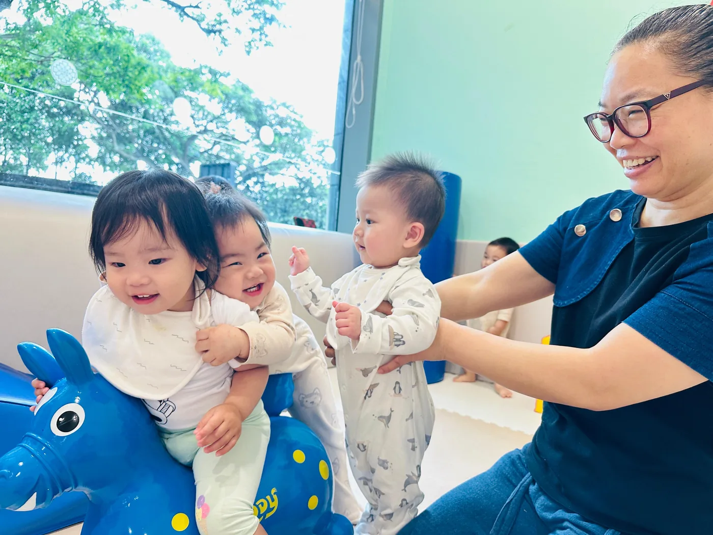 Babies playing by a bright window in a Josiah infant room, an educator steadying one of them