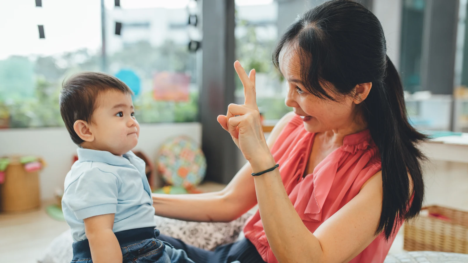 A Josiah educator using a baby sign with a young child in a bright infant room